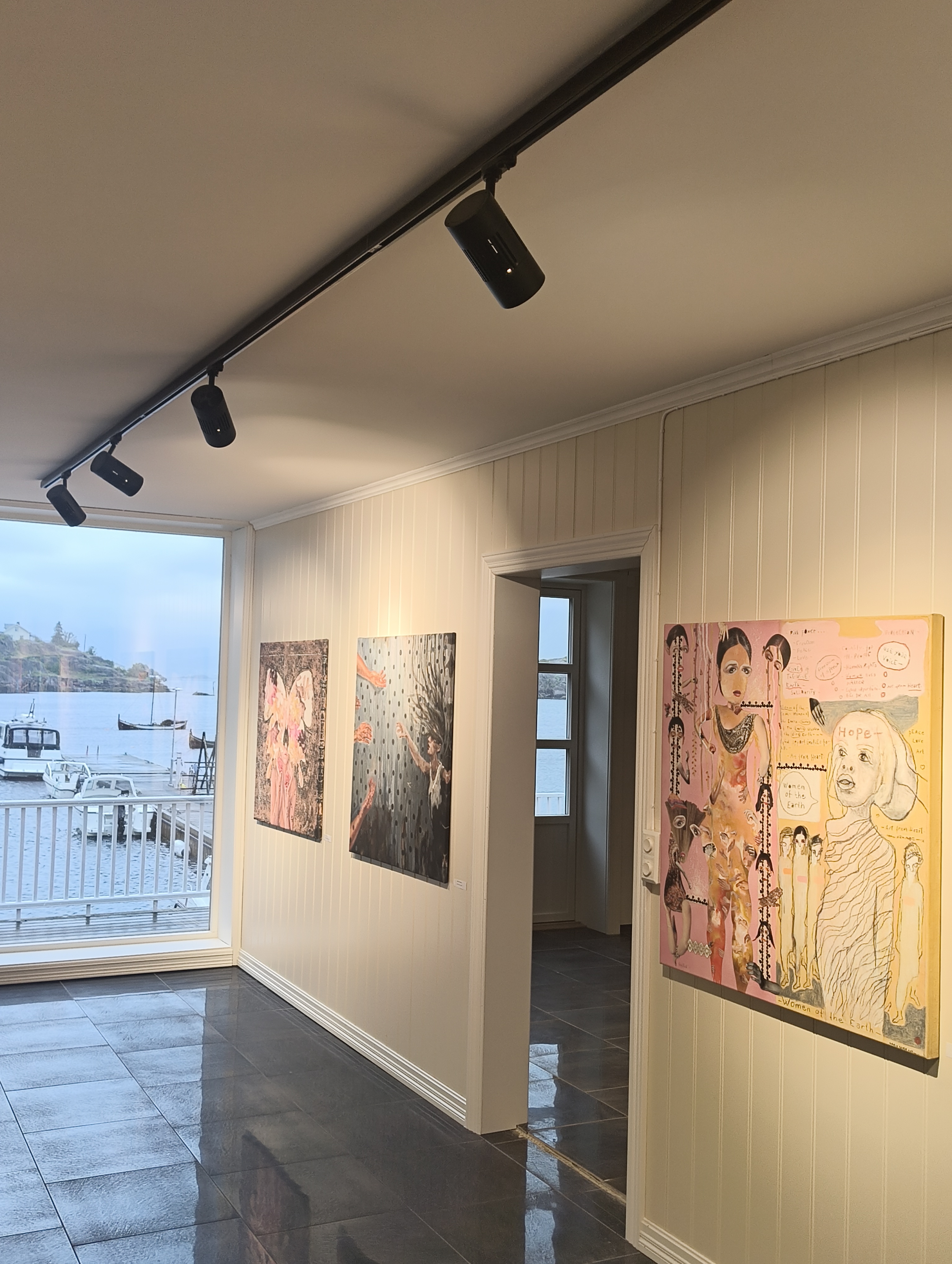 Paintings at Artdom Gallery beside a window onto the sea